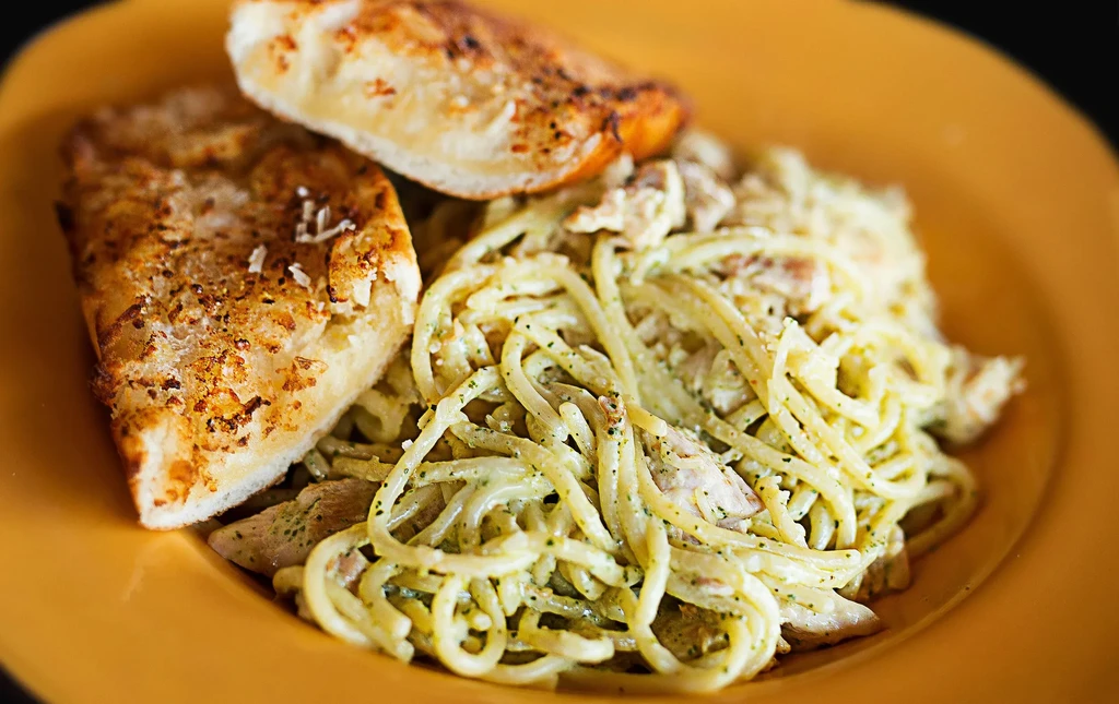 Creamy green sauce pasta with chicken and two slices of garlic bread.