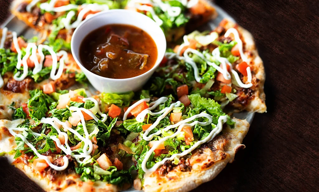 Taco pizza slices with meat, cheese, vegetables, creamy sauce, and salsa.