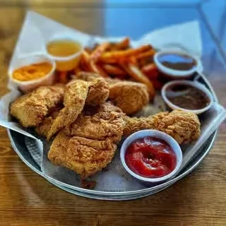 Crispy fried chicken, sweet potato fries, and various dipping sauces on a tray.