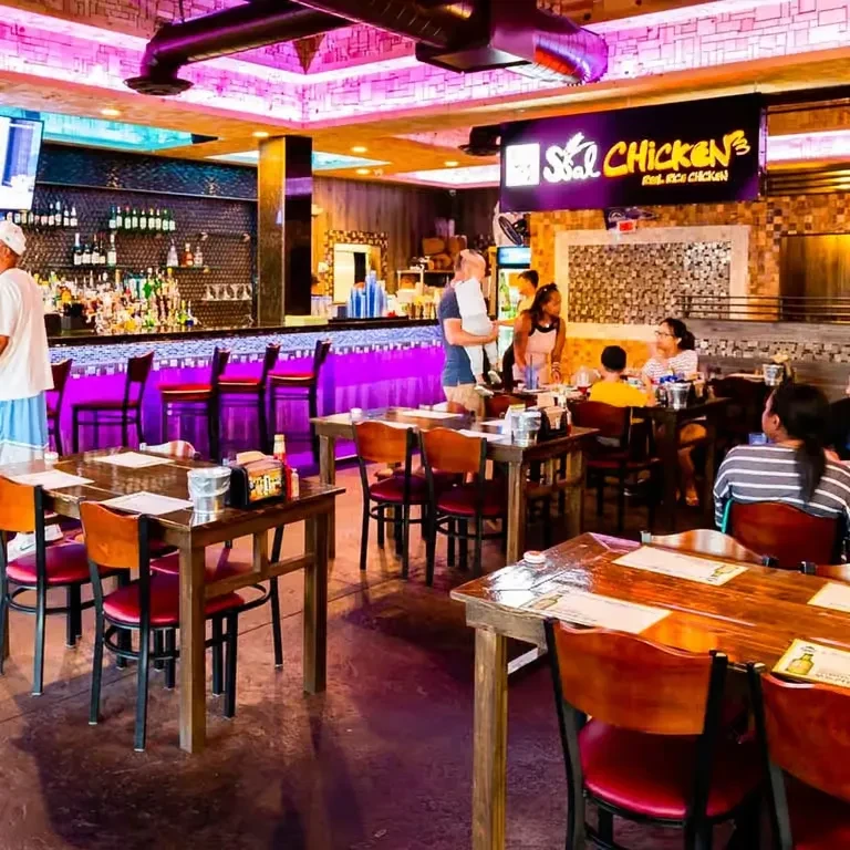 Vibrant restaurant interior with purple neon lighting, a bar, and people dining.