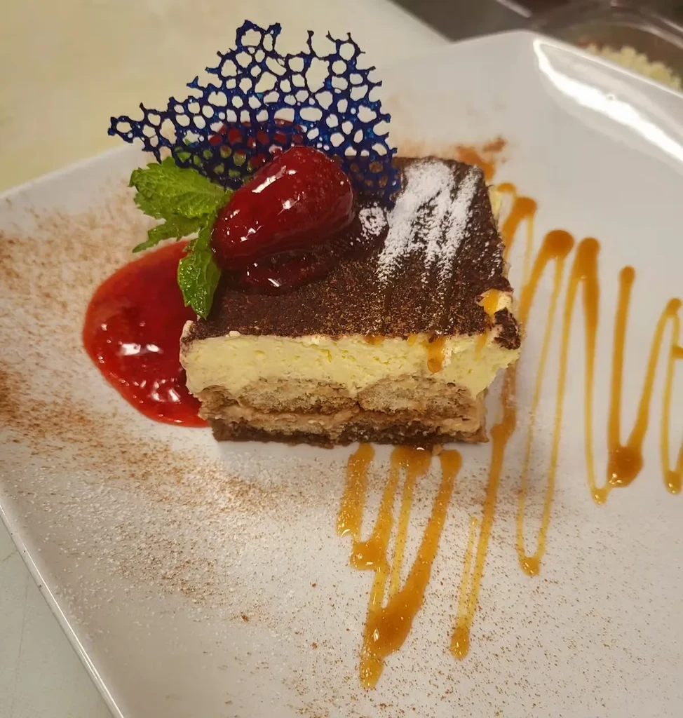Plated tiramisu with strawberry, mint, cocoa, blue tuile, and sauces.