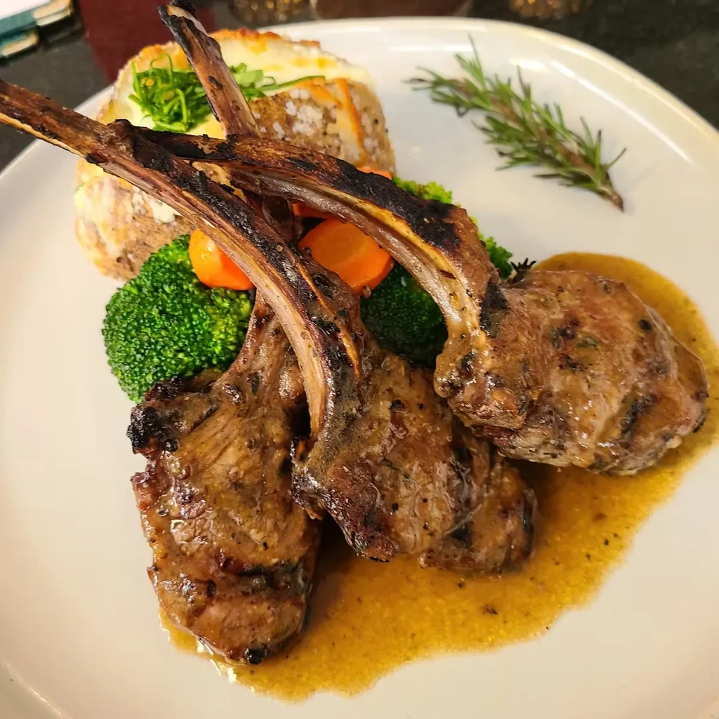 Grilled lamb chops with broccoli, carrots, and a side potato.