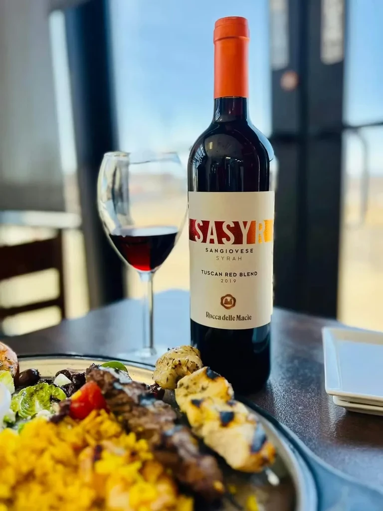 Table with SASYR Tuscan red wine bottle, a glass, and a food plate.