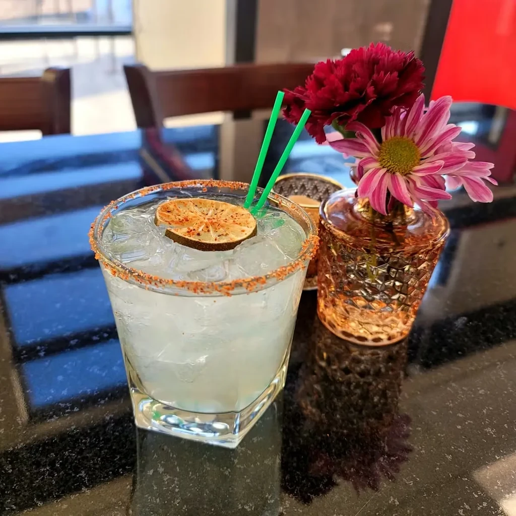 Faceted glass with spiced lime drink, green straws, and flowers.