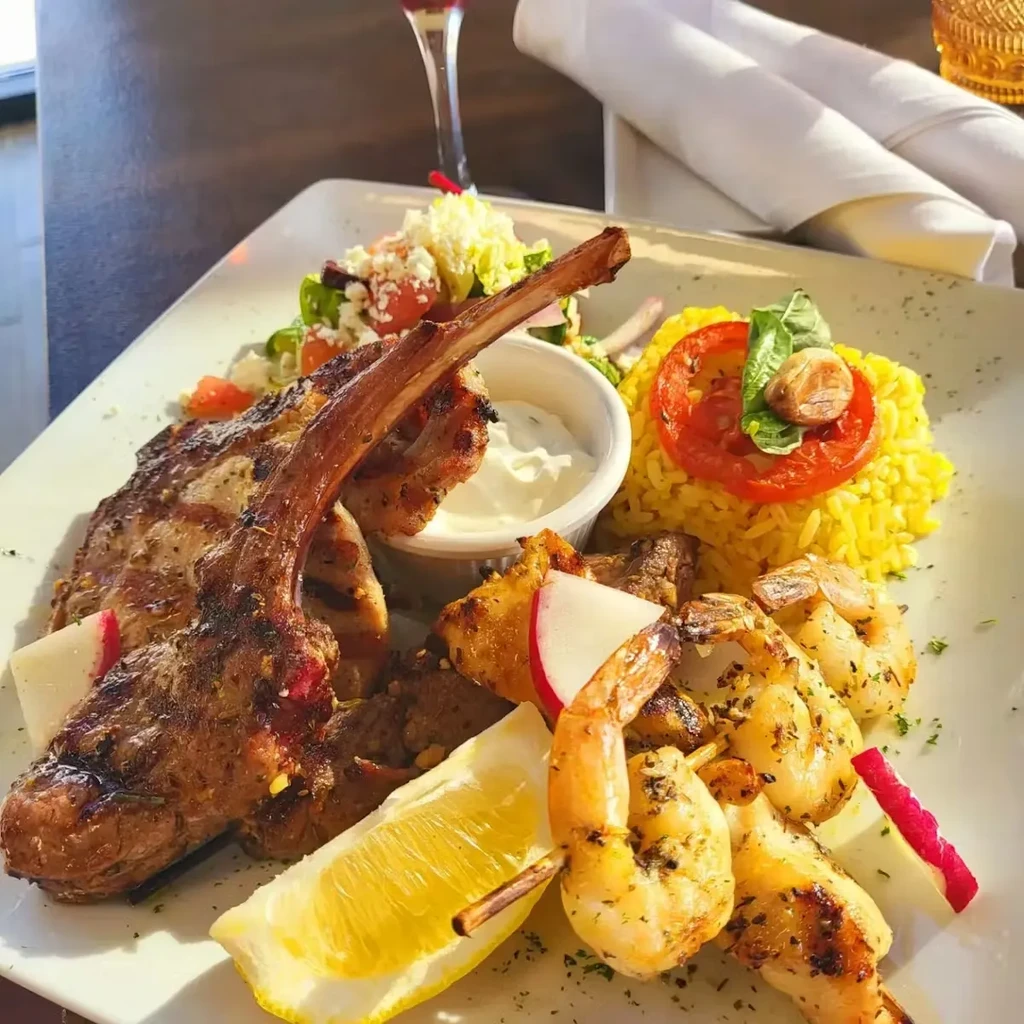 Plated lamb chop, grilled shrimp, yellow rice, salad, creamy sauce.