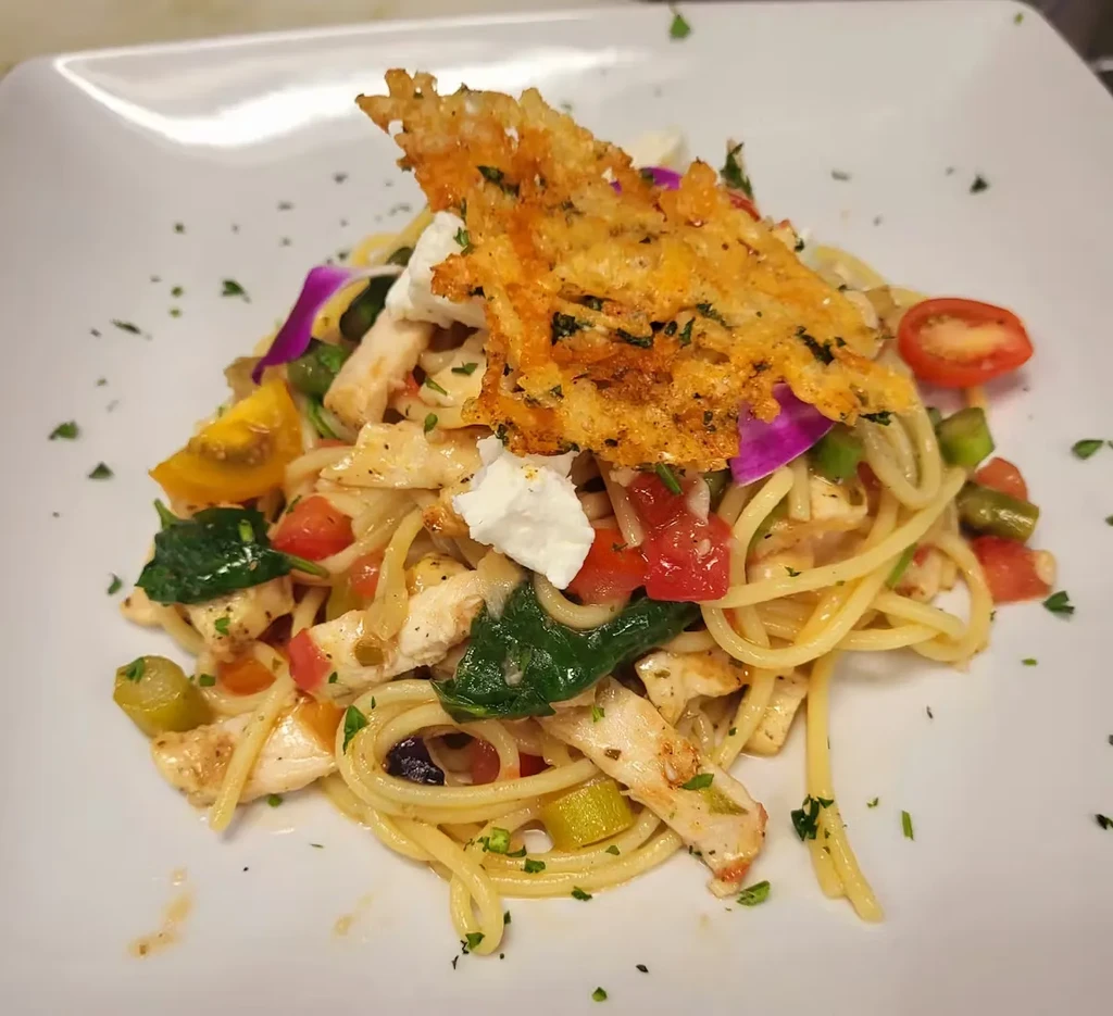 Plated spaghetti with chicken, tomatoes, spinach, feta, and a cheese crisp.