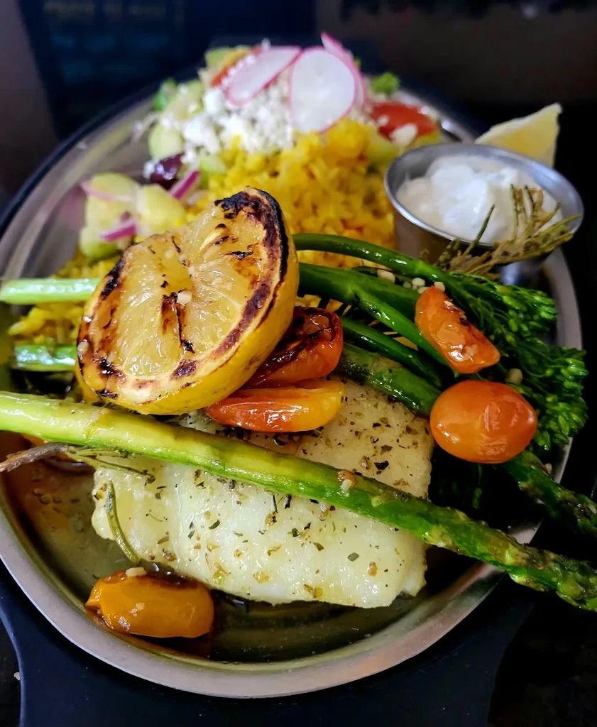 White fish with asparagus, tomatoes, grains, and salad on a platter.
