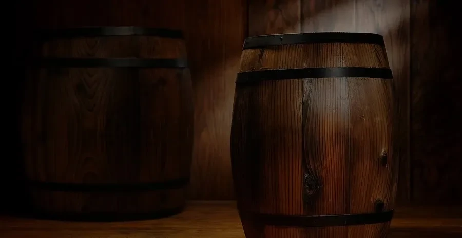 Two wooden barrels, one illuminated, one dark, against wooden planks.