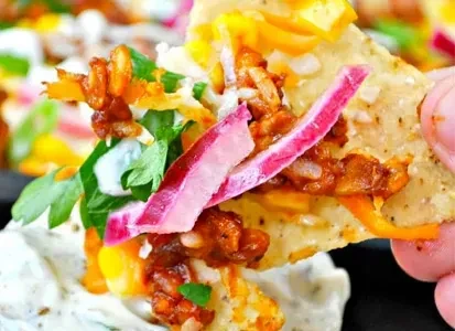 Hand holding a loaded nacho with meat, cheese, onion, dipped in sauce.