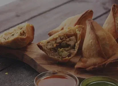 Golden samosas, one cut open to reveal savory filling, with two chutneys.
