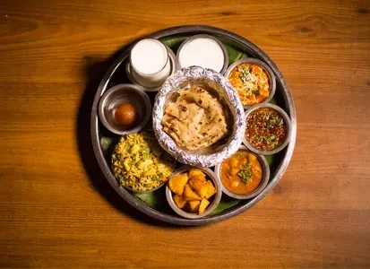 Indian thali meal: flatbread, curries, sweets, and drinks on a wooden table.