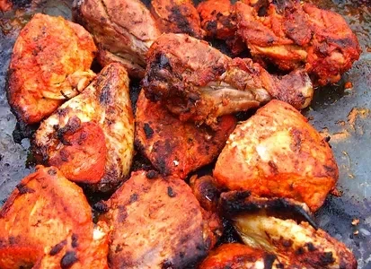Close-up of charred, reddish-orange chicken pieces on a dark griddle.