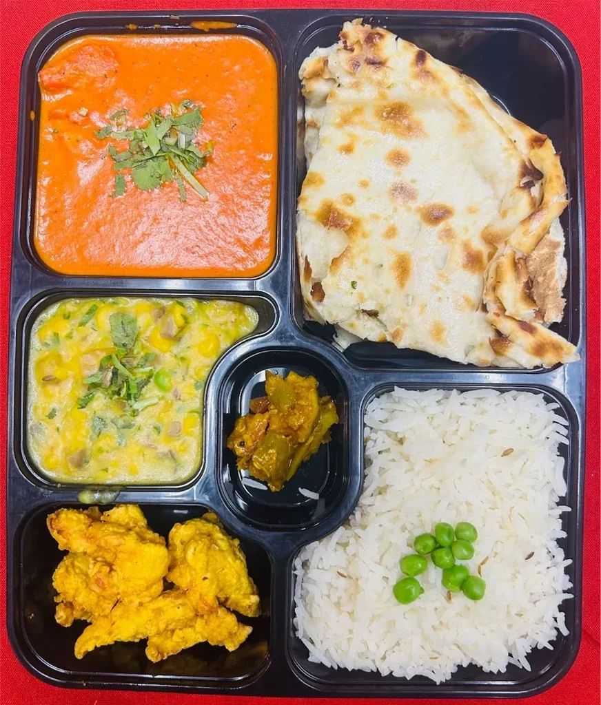 Overhead: six-compartment Indian takeout meal with curries, rice, naan, and fried items.