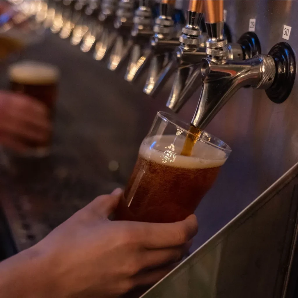 Hands catching golden-brown beer pouring from tap into glass.