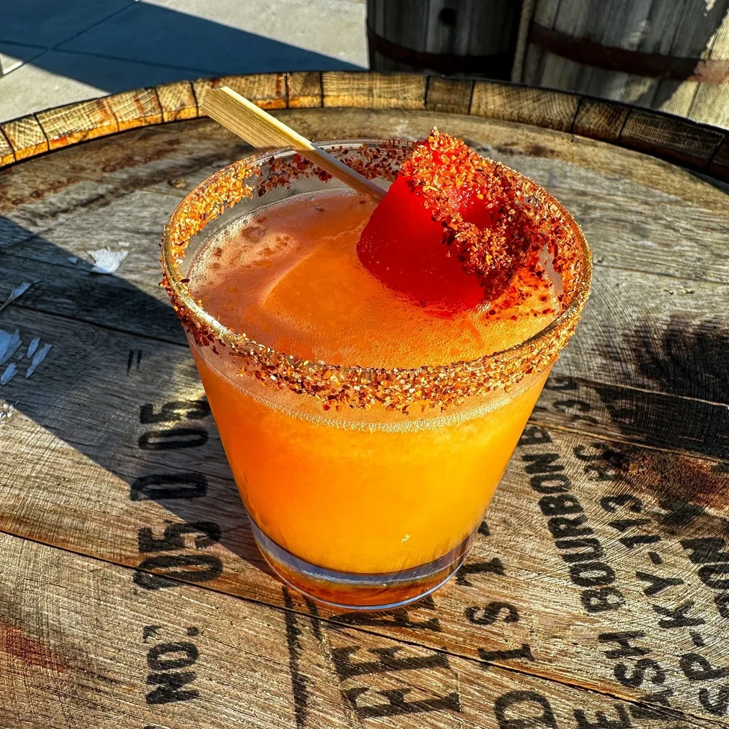 Orange cocktail with seasoned rim and garnish on a bourbon barrel.