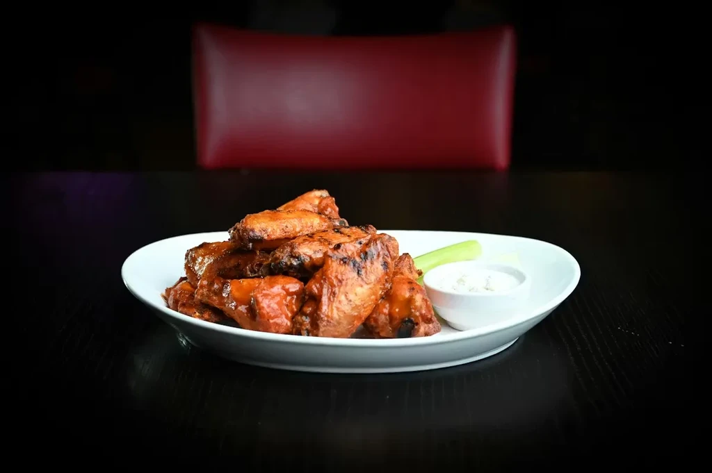 Plate of buffalo chicken wings with dipping sauce and celery.
