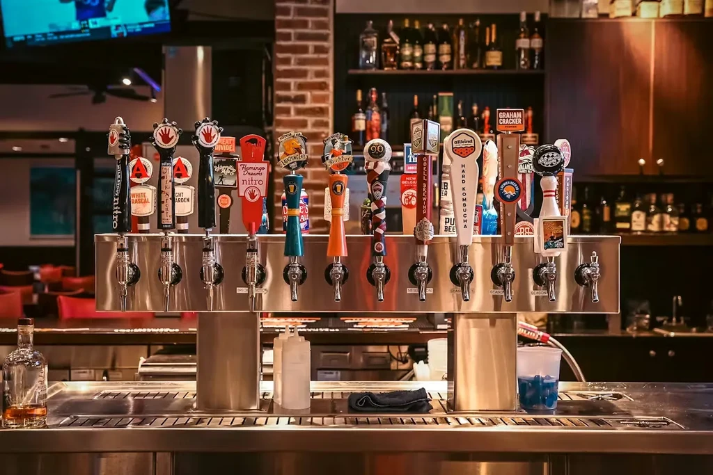 A well-lit bar counter with numerous polished stainless steel beer taps.
