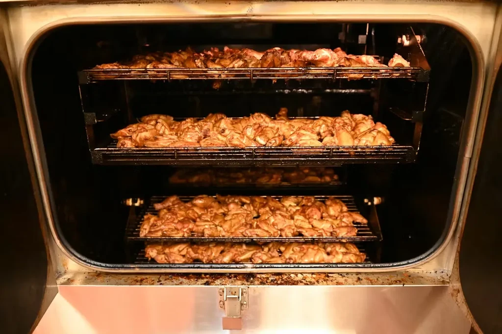 Multiple racks of golden-brown chicken cooking inside a large oven.