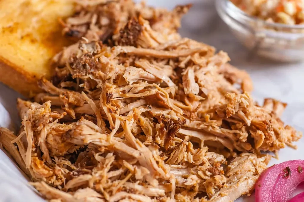 Shredded pulled pork sandwich with toasted bun, coleslaw, and pickled onions.
