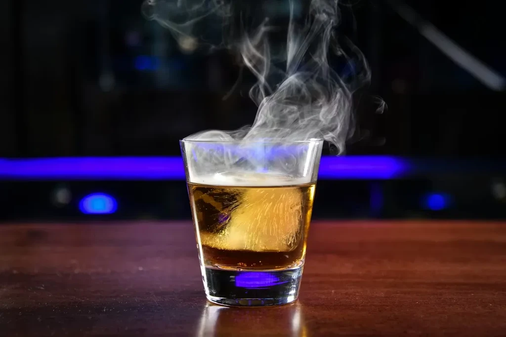 Amber drink with dramatic smoke, large ice, blue background.