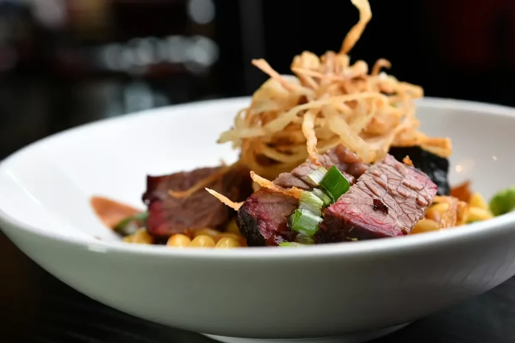 Well-seared beef garnished with crispy onions and green onions.