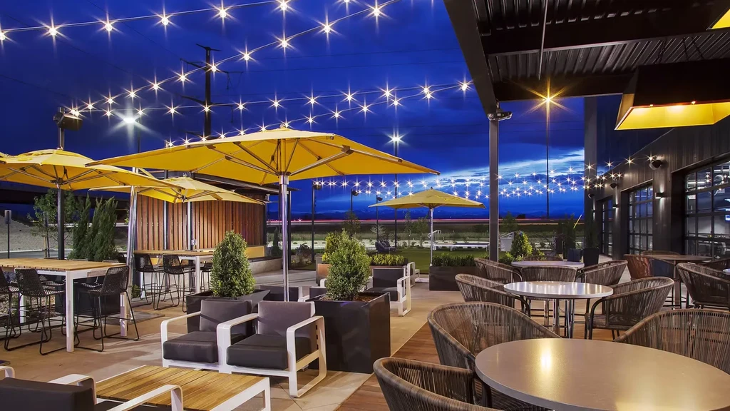 Modern outdoor restaurant patio at dusk with string lights and yellow umbrellas.