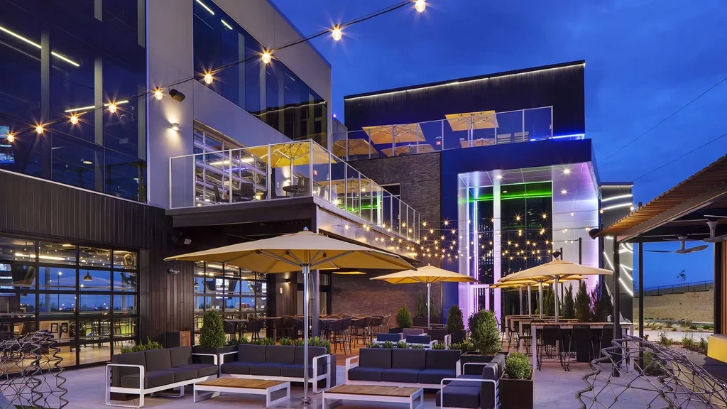 Modern multi-level restaurant patio at dusk with yellow umbrellas and string lights.