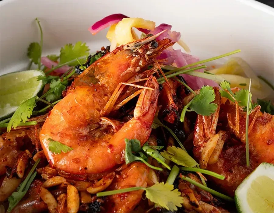Charred prawns in white bowl with cilantro, red onion, and lime.