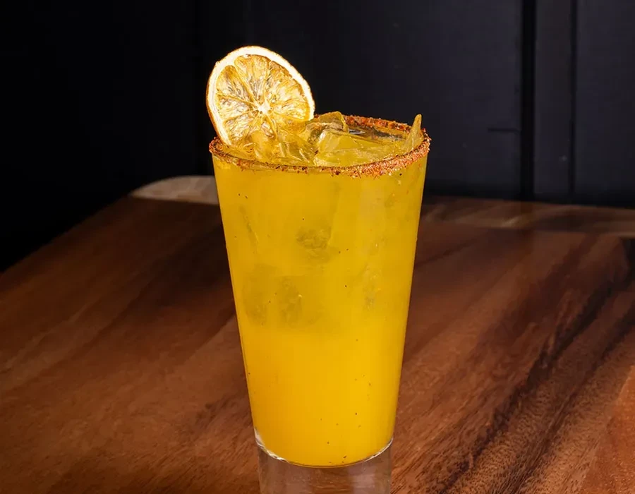 Yellow drink in a glass with ice, spice rim, and dried citrus.