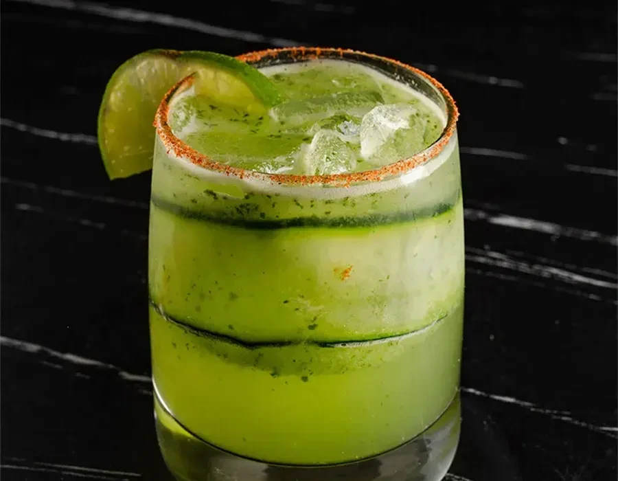 Vibrant green drink, seasoned rim, lime wedge, and ice.