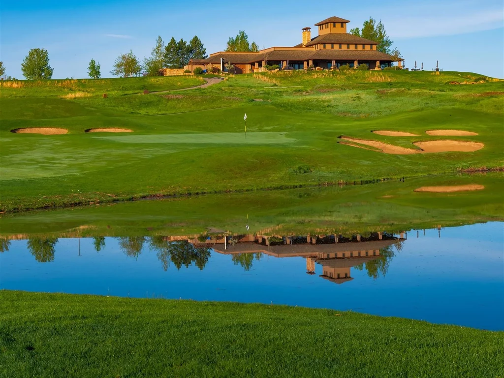 Multi-story lodge on a green hill, golf course, pond reflection.