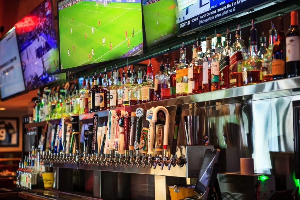 Well-stocked bar with liquor bottles, beer taps, and multiple sports TVs.
