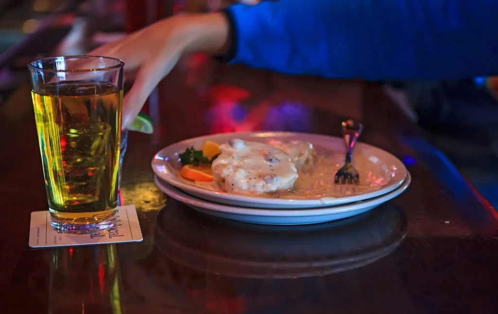 Hand reaching for beer and biscuits with gravy on counter.