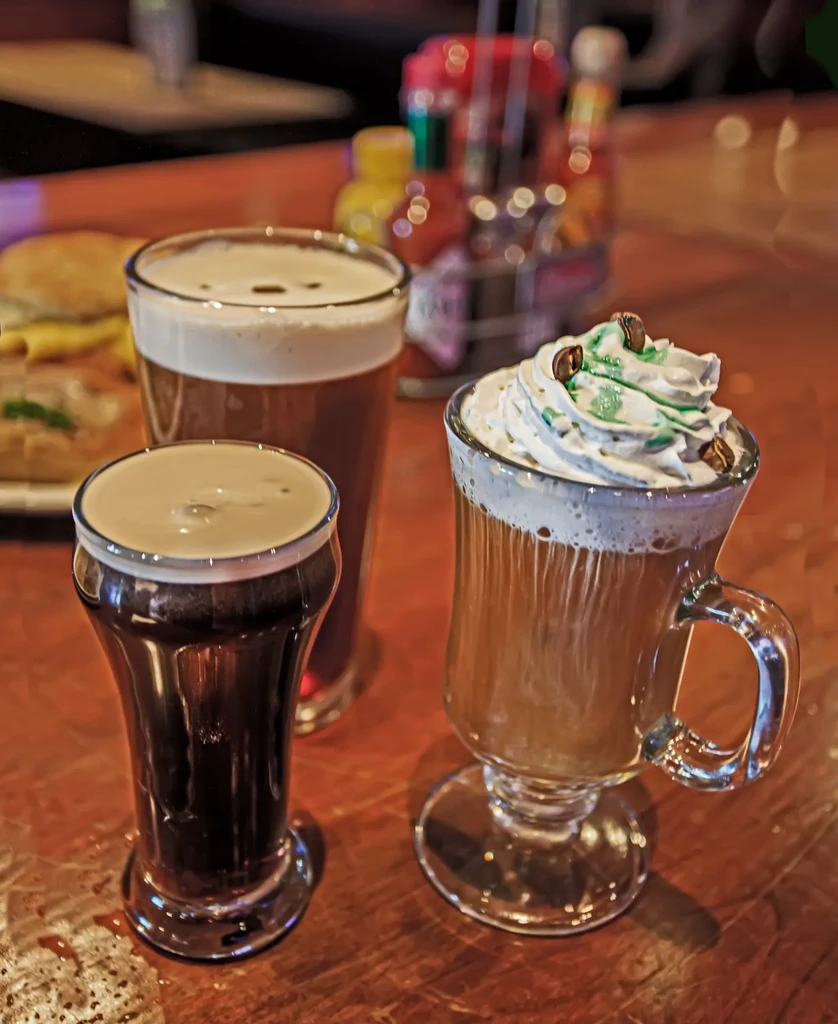 Three distinct beverages with foam and whipped cream on a wooden table.