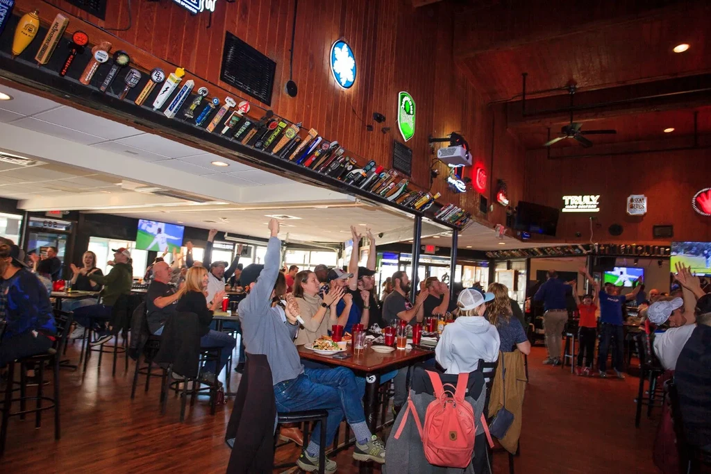 Vibrant sports bar: patrons cheer at event on multiple TVs.