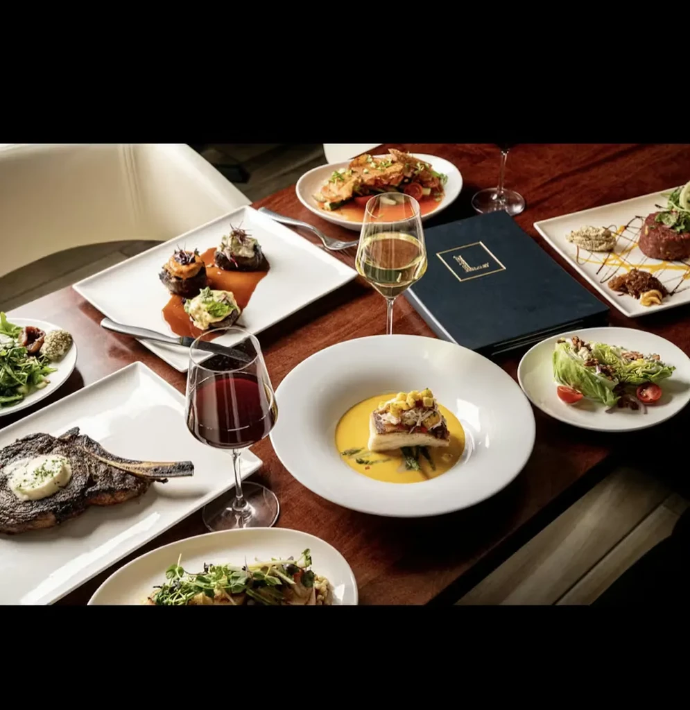 Fine dining table with steak, fish, salads, wines, and a menu.