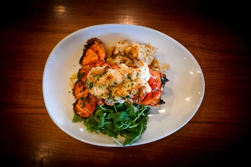 Top-down view of grilled lobster, leafy greens, and creamy side dish.