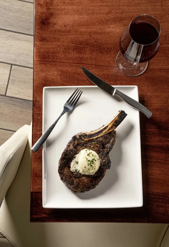 Overhead view of grilled steak, herb butter, red wine, silverware.