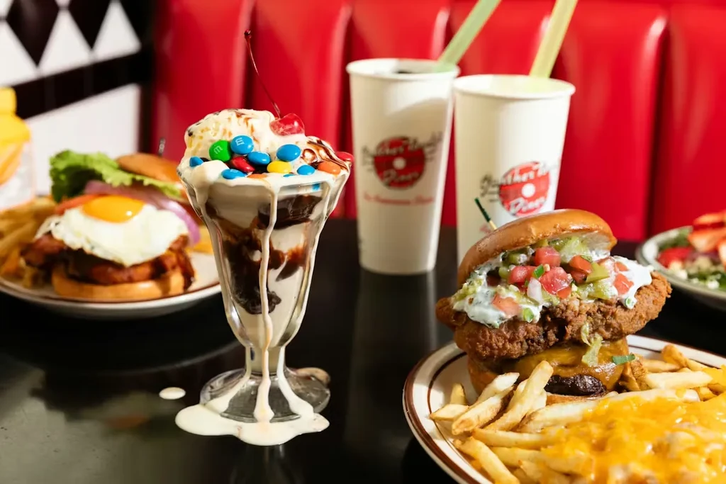 Overflowing sundae, elaborate burger, and cheesy fries on a diner table.