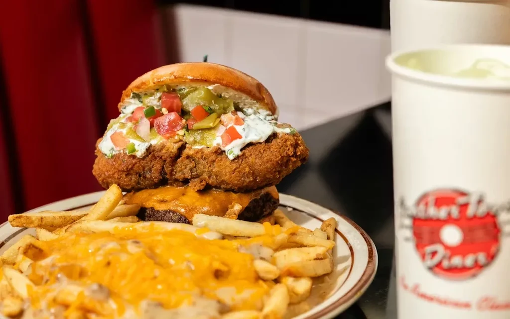 Towering fried patty and cheeseburger, cheesy fries, and a diner drink.