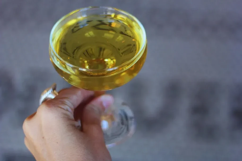 Hand with ring holds coupe glass filled with golden-yellow drink.