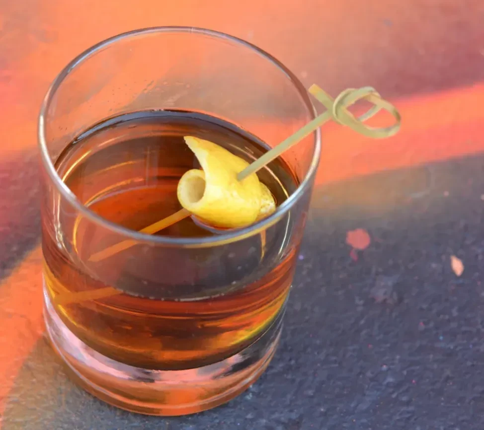 Amber cocktail in a rocks glass with a twisted lemon peel.