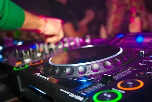 DJ's hands adjust controls on an illuminated professional mixing console.