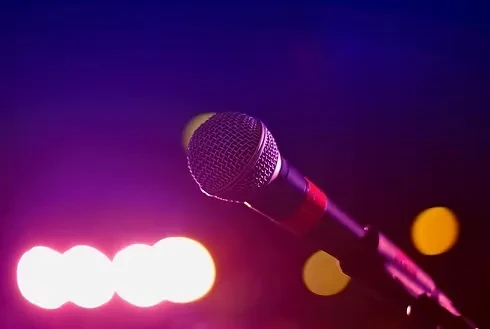 Microphone on stand against blurred purple, magenta, and blue stage lights.