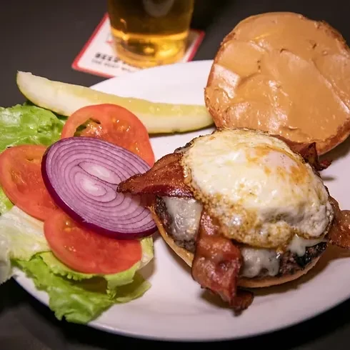 Open-faced gourmet burger, bacon, fried egg, melted cheese, salad, pickle.