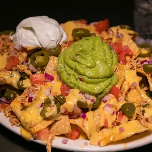 Loaded nachos with melted cheese, meat, jalapeños, guacamole, and sour cream.