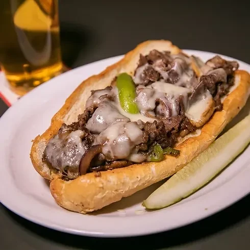Cheesesteak with onions, peppers, melted cheese, and a pickle.