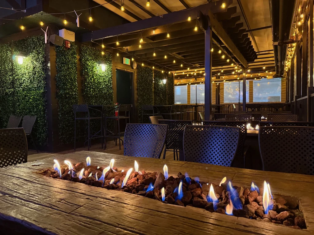 Restaurant patio with a wooden fire pit table under string lights.
