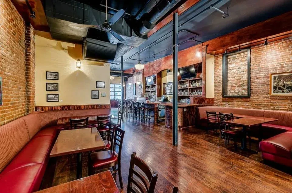 Industrial-chic restaurant interior with exposed brick, bar, and red banquettes.