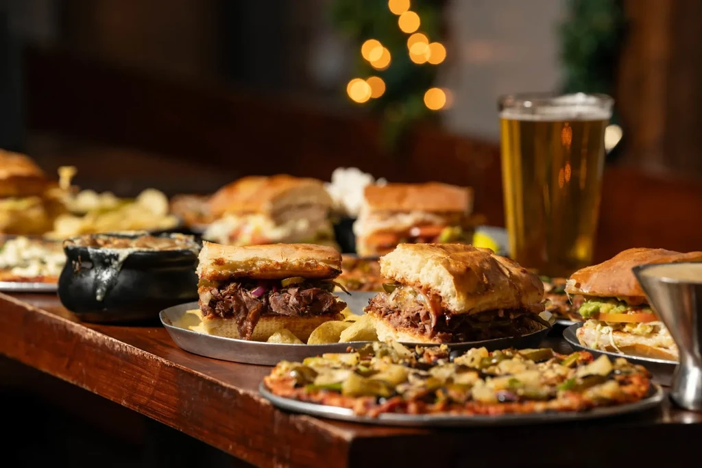 Pizza, sandwiches, stew, and beer arranged on a dark wooden table.
